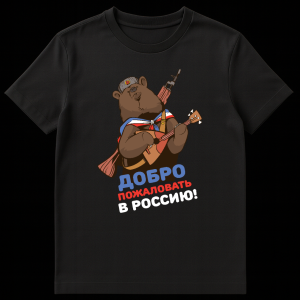 T-shirt mockup featuring a cartoon brown bear wearing a red star ushanka and Russian flag scarf, playing a balalaika with an AK-47 on its back. The text "ДОБРО ПОЖАЛОВАТЬ В РОССИЮ!" is below. on black t-shirt
