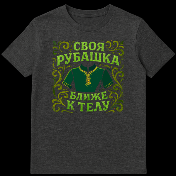 Close-up of a t-shirt featuring a stylized dark green Russian rubakha with yellow trim, surrounded by green and yellow swirling floral motifs, and the Russian proverb 'SVOYA RUBASHKA BLIZHE K TELU' in textured green font. on dark heather t-shirt